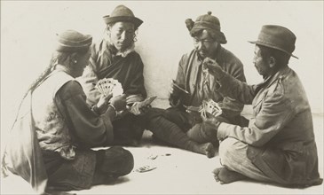 Rickshaw drivers enjoy a game of cards. Four rickshaw drivers sit cross-legged in a circle on the