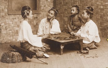Burmese women rolling cheroots. Three young Burmese women kneel around a low table as they roll