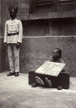 Petty criminal in the stocks, Hong Kong. A petty criminal sits with his ankles restrained in
