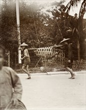 Usual method of carrying a pig'. Two Chinese men carry a pig in a wicker cage suspended from a pole