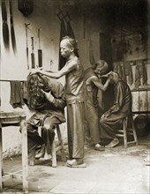 Inside a Chinese barber's shop. Two men with distinctive Manchu hairstyles receive treatment at a