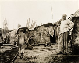Settlement on the banks of the Yangtze River. People mill about at a settlement containing several