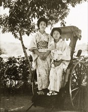 Geisha posing on a rickshaw. Portrait of two geisha from a tea house. They sit side-by-side on a
