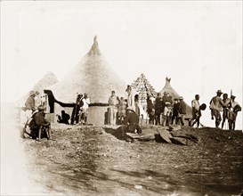 Matabele men at Cecil Rhodes' farm. Matabele (Ndebele) men mill about beside a cluster of thatched