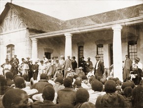 An indaba at Government house. A group of British administrators stand before a seated audience of