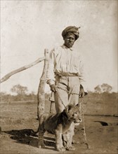 Servant with a pet lion cub. A turbaned servant poses for the camera, holding the chain leash of a
