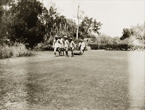 Indian servants gardening. Four Indian servants pull a roller over a tidy lawn, while a fifth man