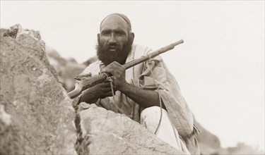 Portrait of an armed Afridi man. Portrait of an armed Afridi man, crouched behind a rock at Kohat