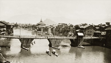 The Jhelum River at Srinagar. Several shikaras pass beneath a wooden road bridge spanning the