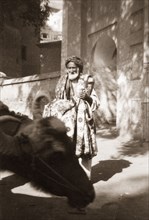 An Indian rug vendor. An elderly street trader touts a variety of patterned rugs as he wanders