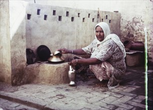 An Indian woman prepares to cook. A women squats beside a stone wall, preparing to cook with a