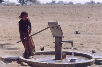 Raising water from a borewell. A young girl operates a hand pump to raise water from a borewell.
