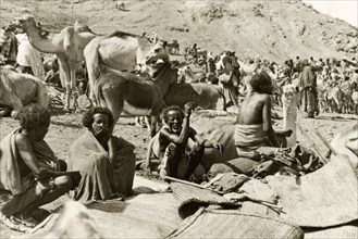Eritrean men at a camel market. Four Eritrean men sit beside a heap of woven mats at a bustling