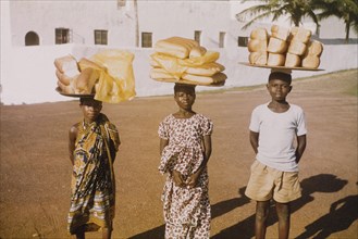 Breadsellers outside Elmina Castle. Three breadsellers pose for the camera, balancing large trays