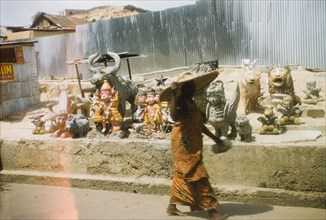 Ornaments at a roadside stall. A woman wearing a wide-brimmed sun hat passes by a roadside stall