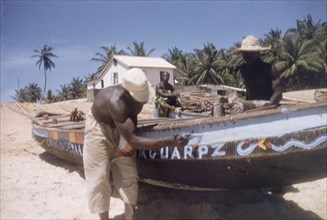 Painting canoes on Prampram beach. Men paint fishing canoes on the beach at Prampram. Near Accra,