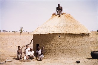 Roof thatcher in northern Ghana. A roof thatcher sits atop a round mud hut in Kuka. Thatchers in