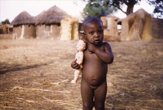 Ghanaian toddler with a European-style doll. Portrait of a naked young girl, aged about three,