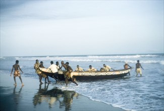Beaching a boat in Saltpond. A group of men haul a painted fishing boat out of the sea and onto the