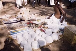 Hat seller at Tamale market. A market trader sits on a woven mat on the ground, selling hats and