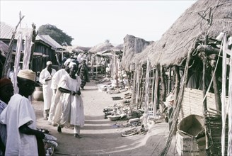 A marketplace in Kano. Stalls with thatched canopies shelter goods from the sun in a busy