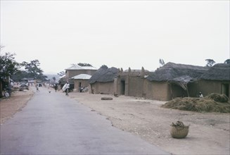 Main road through a Hausa village. Low, mud-walled buildings flank the main road running through a