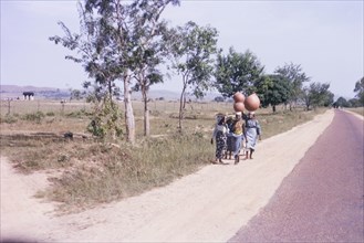 Nigerian women carrying pots. A small group of Nigerian women walk along a roadside carrying large