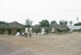 A Hausa village. Inhabitants of a Hausa village mill about outside several square, mud-walled huts