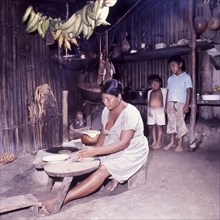 Preparing tortillas, Belize. A Ketchi woman sits at a low table indoors, preparing tortillas under