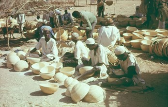 Hausa potters decorating bowls. A group of Hausa potters sit outdoors, using metal tools to