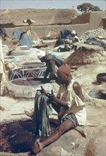 Hausa man dyeing fabric. A Hausa man sits beside a well of liquid dye, carefully dipping a section