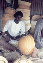 A Hausa potter decorates a bowl. A Hausa potter uses a metal tool to inscribe patterns onto a clay
