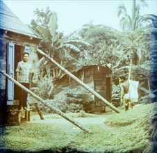 Rural housing in Dominica. A Dominican man stands in the doorway of a wooden house on stilts as a