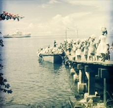 Maritime trade, Dominica. A group of women walk along a wooden pier carrying sacks on their heads,