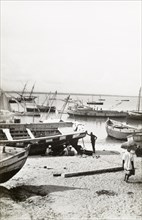 Dry-docked boats in Lamu harbour. A group of men sit on a beach beside a dry-docked boat in Lamu