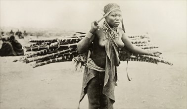 Kikuyu woman carrying canes. A Kikuyu woman carries a bundle of canes on her back, supported by a