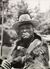 Chief Murigo. Portrait of Chief Murigo wearing traditional Kikuyu jewellery and holding a staff. He