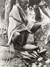 Reading the beans'. A witch doctor prepares to tell the fortune of a client, using beans contained