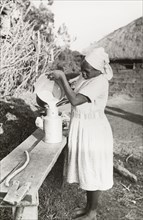 Kikuyu woman pouring milk. A Kikuyu woman, wearing a Western-style dress and headscarf, pours milk