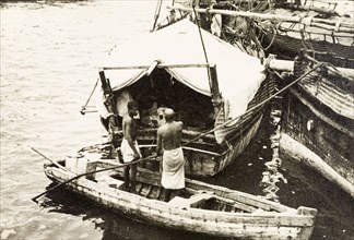 Attending to cargo at Old Mombasa harbour. Two men stand in a canoe, attending to cargo stored