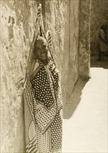 Wrapped in a swathe of fabric. An elderly person leans against a wall in Lamu, wrapped in a swathe