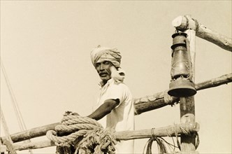 Sailor with a seabird. A turbaned dhow captain stands on the deck of his boat with a seabird