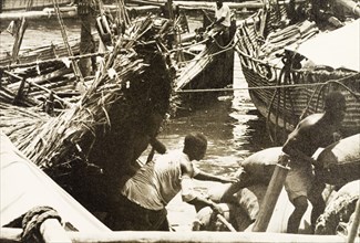 Unloading cargo at Old Mombasa harbour. Men unload cargo from beneath the thatched canopy of a dhow