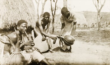 Pouring drinks from a gourd. A Kenyan man pours his two friends a drink from a gourd, one of whom