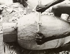 Carving the shell of an atumpan drum. A craftsman uses a long blade to carve the shell of an