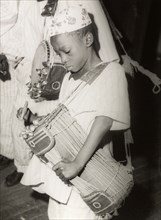 Child playing a 'dundun' drum. A child plays a 'dundun' (talking drum), a double-headed drum shaped