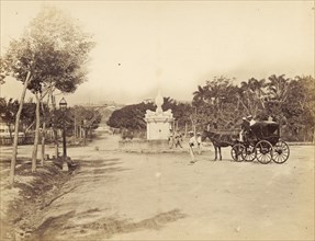 A road junction in Cuba. A horse-drawn coach approaches an empty road junction with a monument at