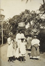 Returning from market, Tobago. A group of women and girls return from a local market balancing