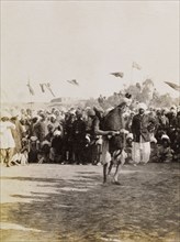 Lifting a blindfolded donkey. A man struggles to lift a blindfolded donkey in front of a crowd of