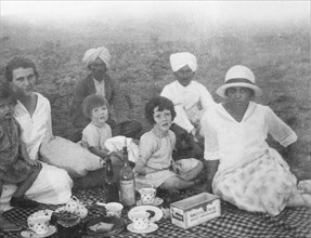 A family picnic in India. A British family enjoys a picnic outdoors, accompanied by three Indian